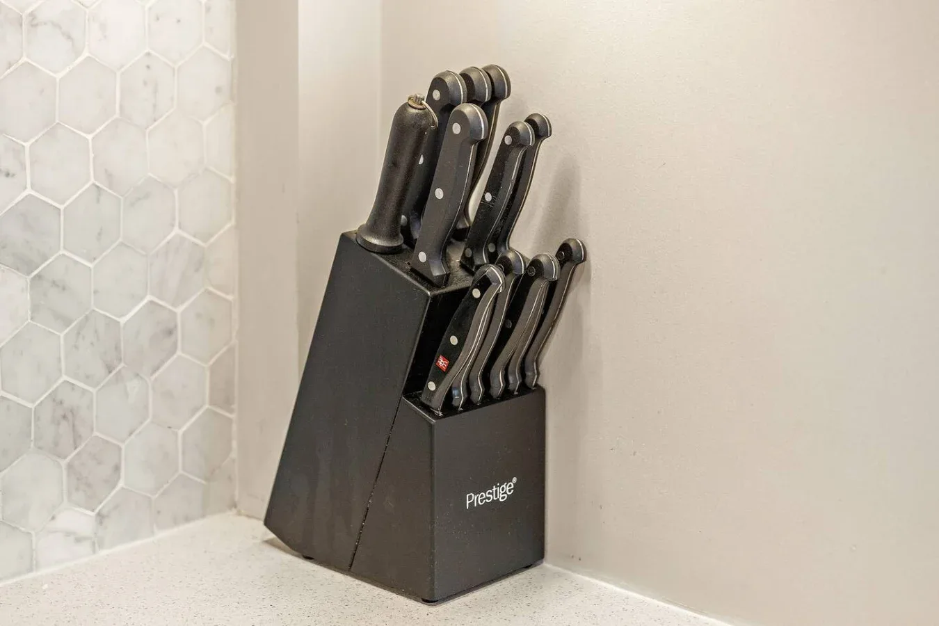 Una encimera de cocina con un bloque negro de cuchillos junto a un revestimiento de azulejos hexagonales.