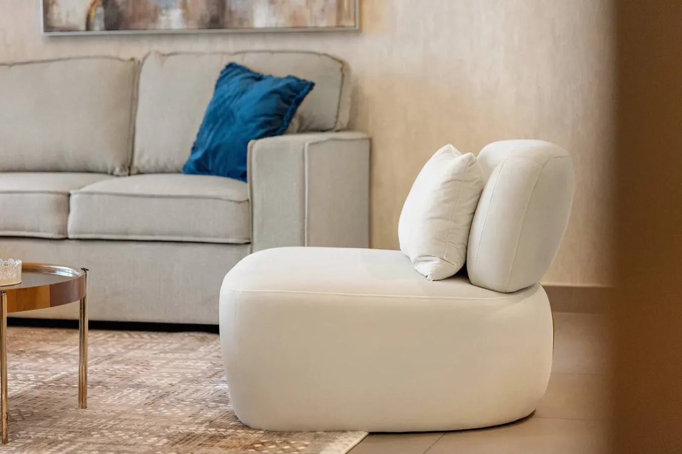 Una sala de estar con un sofá beige y un asiento tapizado redondeado.