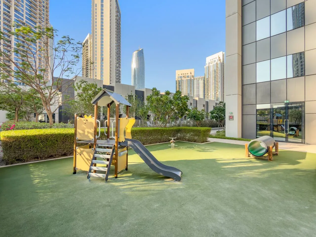 Un parque infantil al aire libre con una estructura de juego y un tobogán entre edificios altos.