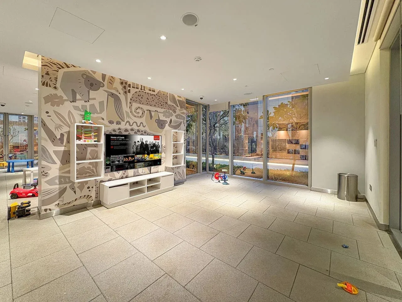 Una luminosa zona de juegos interior tiene un mural, estantes con juguetes y grandes ventanas.