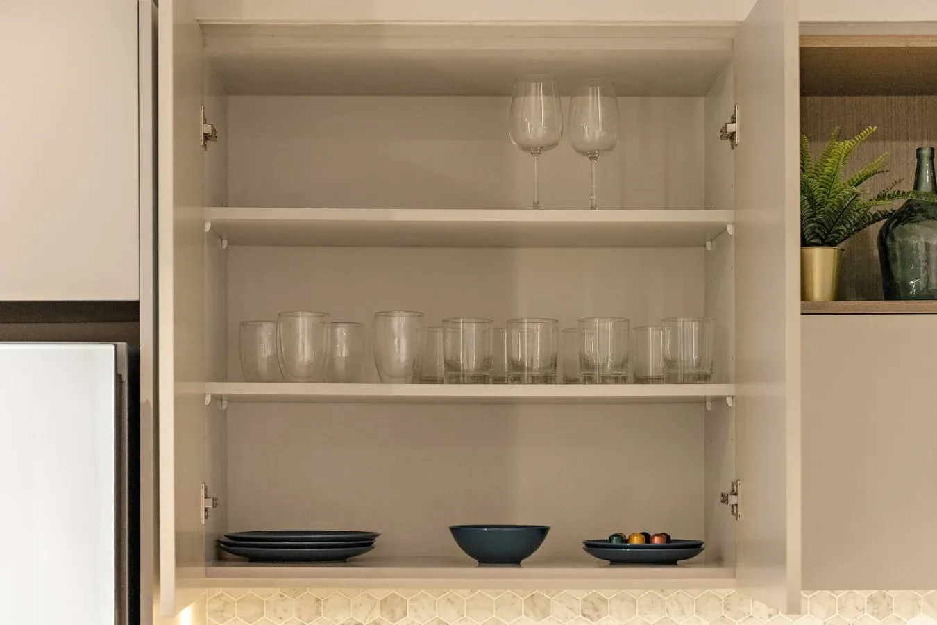 Un armario de cocina abierto muestra copas, vasos y platos.