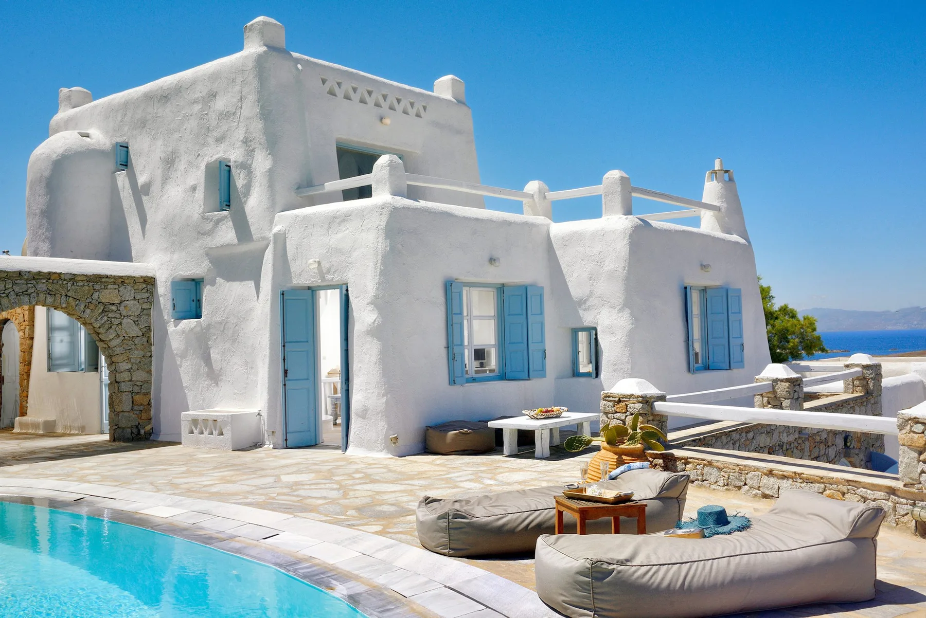 Una villa blanca de estilo mediterráneo con contraventanas azules da a una piscina.