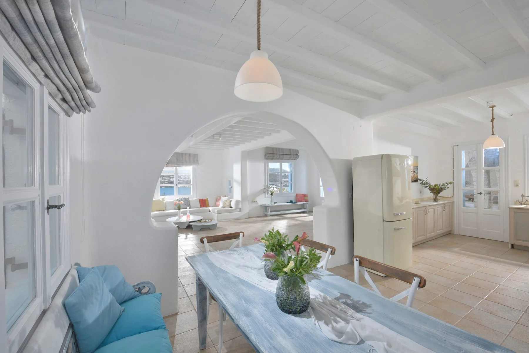 Una luminosa cocina y comedor con una mesa larga y asientos azules.