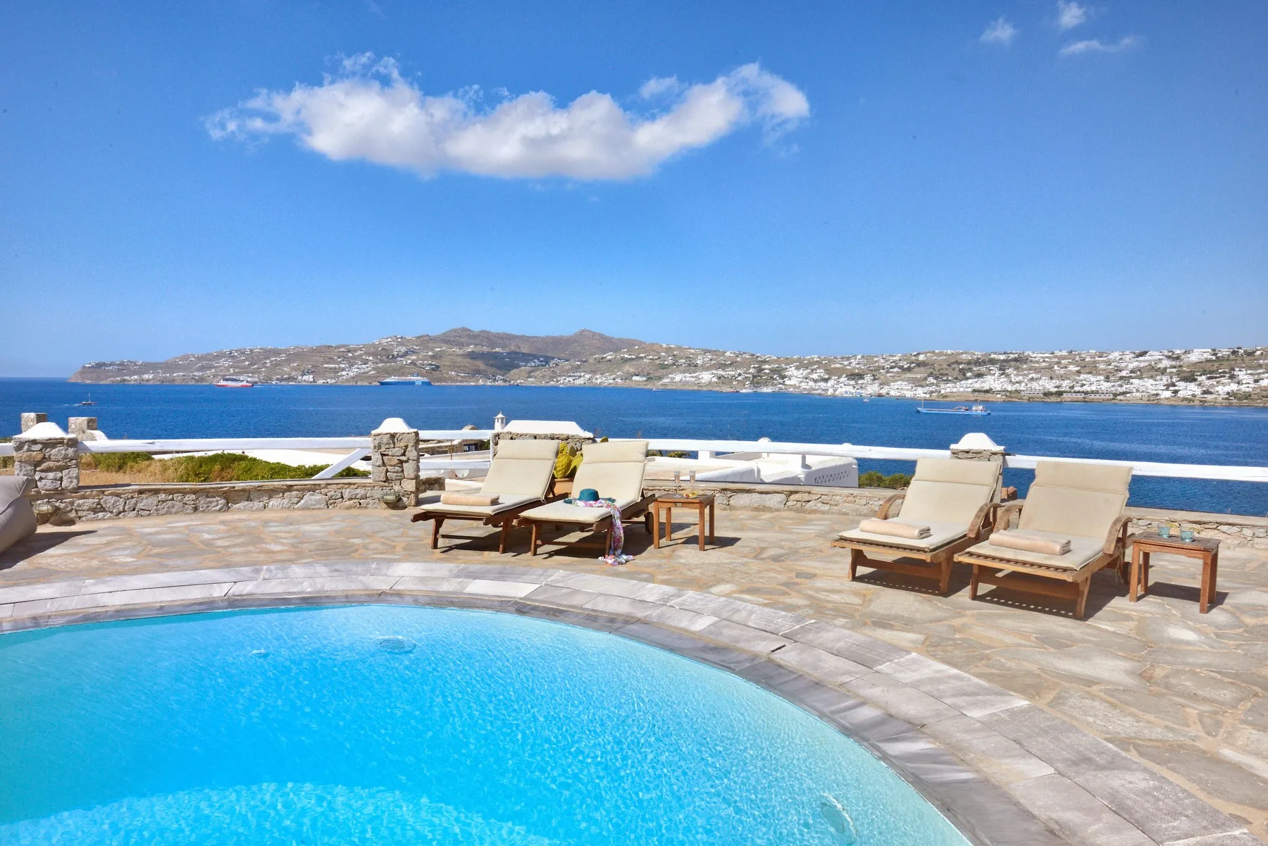 Una piscina y tumbonas miran al mar y a la costa a lo lejos.
