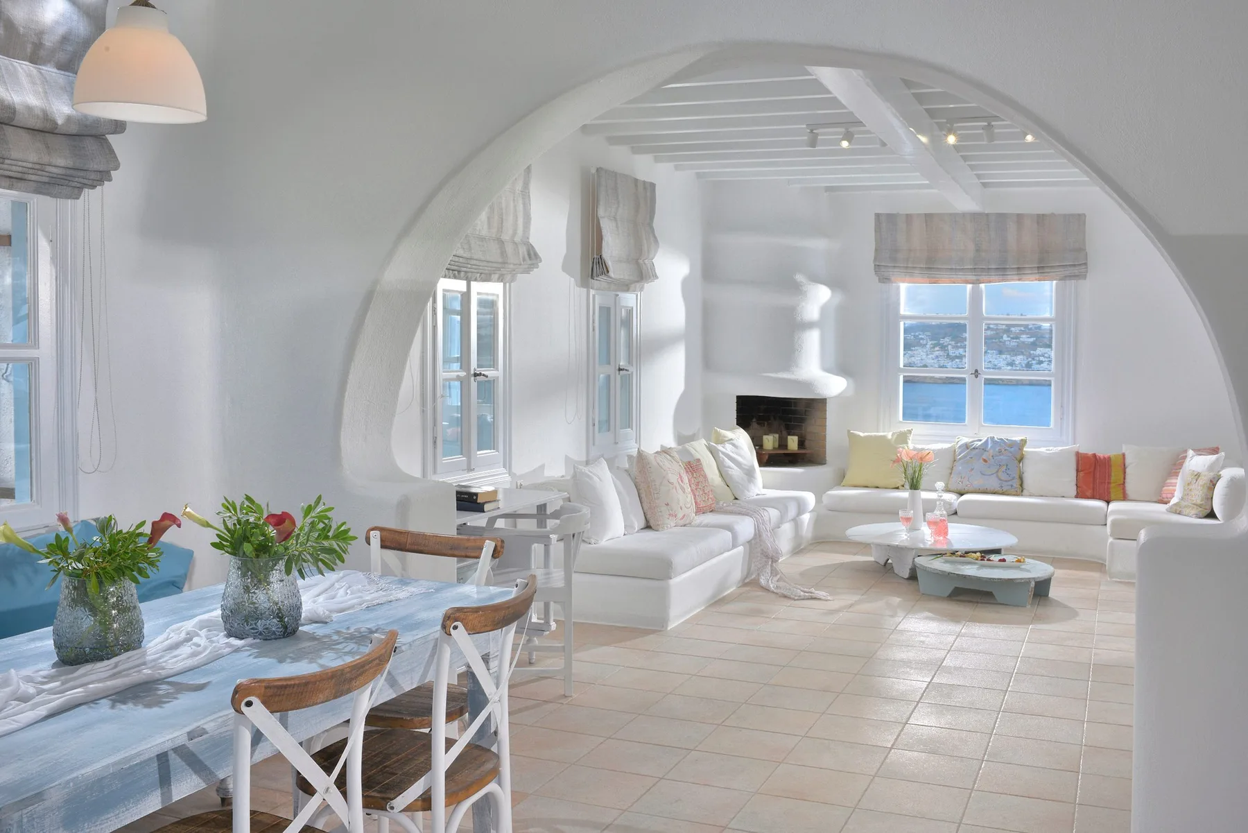 Una sala luminosa con asientos blancos y una mesa de comedor junto a las ventanas.