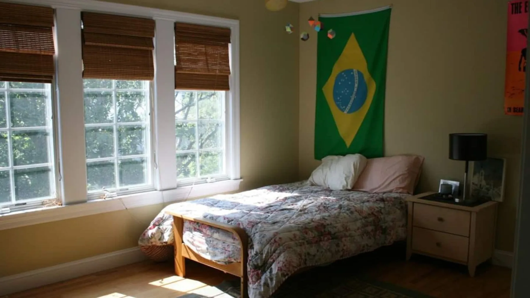 A bedroom with a bed beside three windows with wooden blinds.