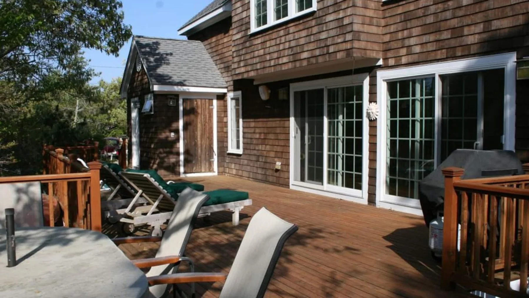 A wooden deck beside a house has patio seating and large glass doors.