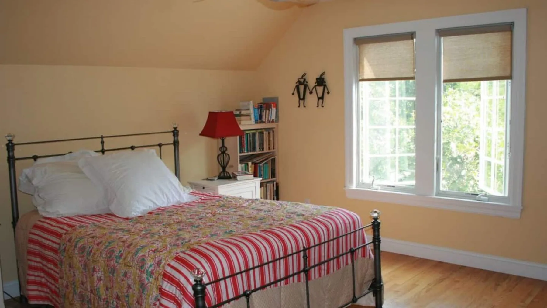 A bedroom with a metal bed, colorful bedding, and two windows.