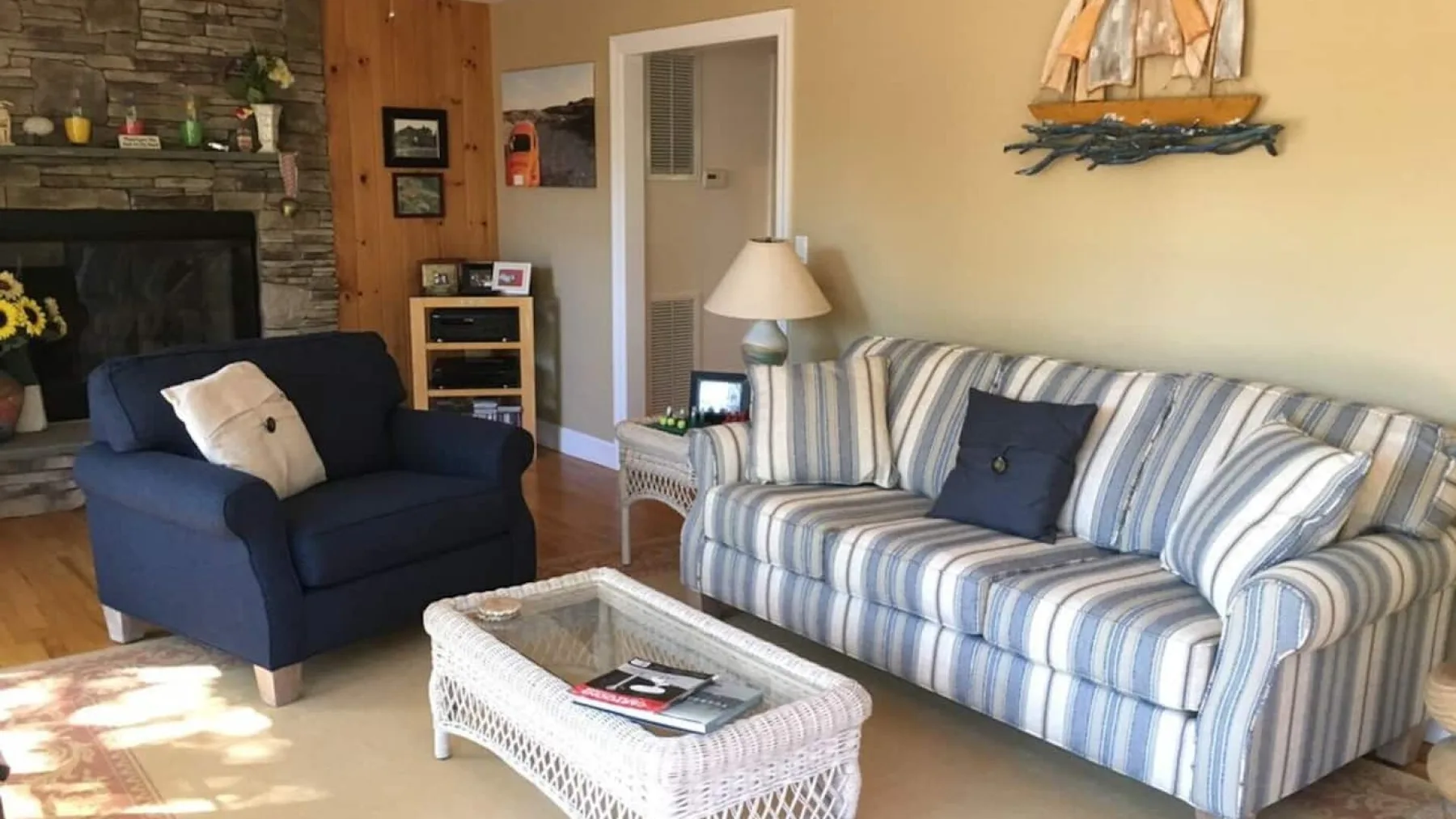 A living room with striped seating, a stone fireplace, and a woven coffee table.