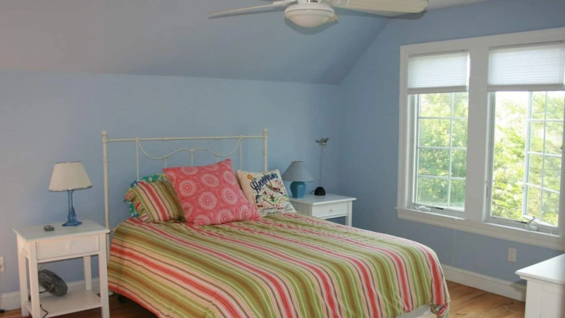 A bedroom with a bed covered in colorful striped bedding beside large windows.