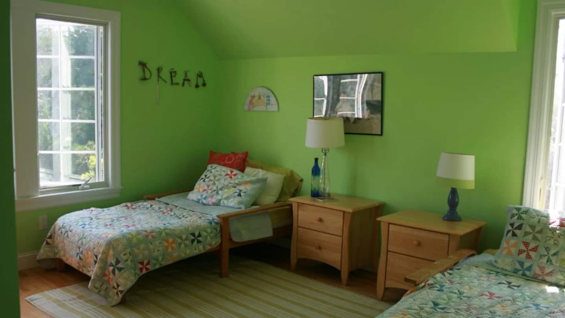 A green bedroom with two beds, wooden nightstands, and windows.