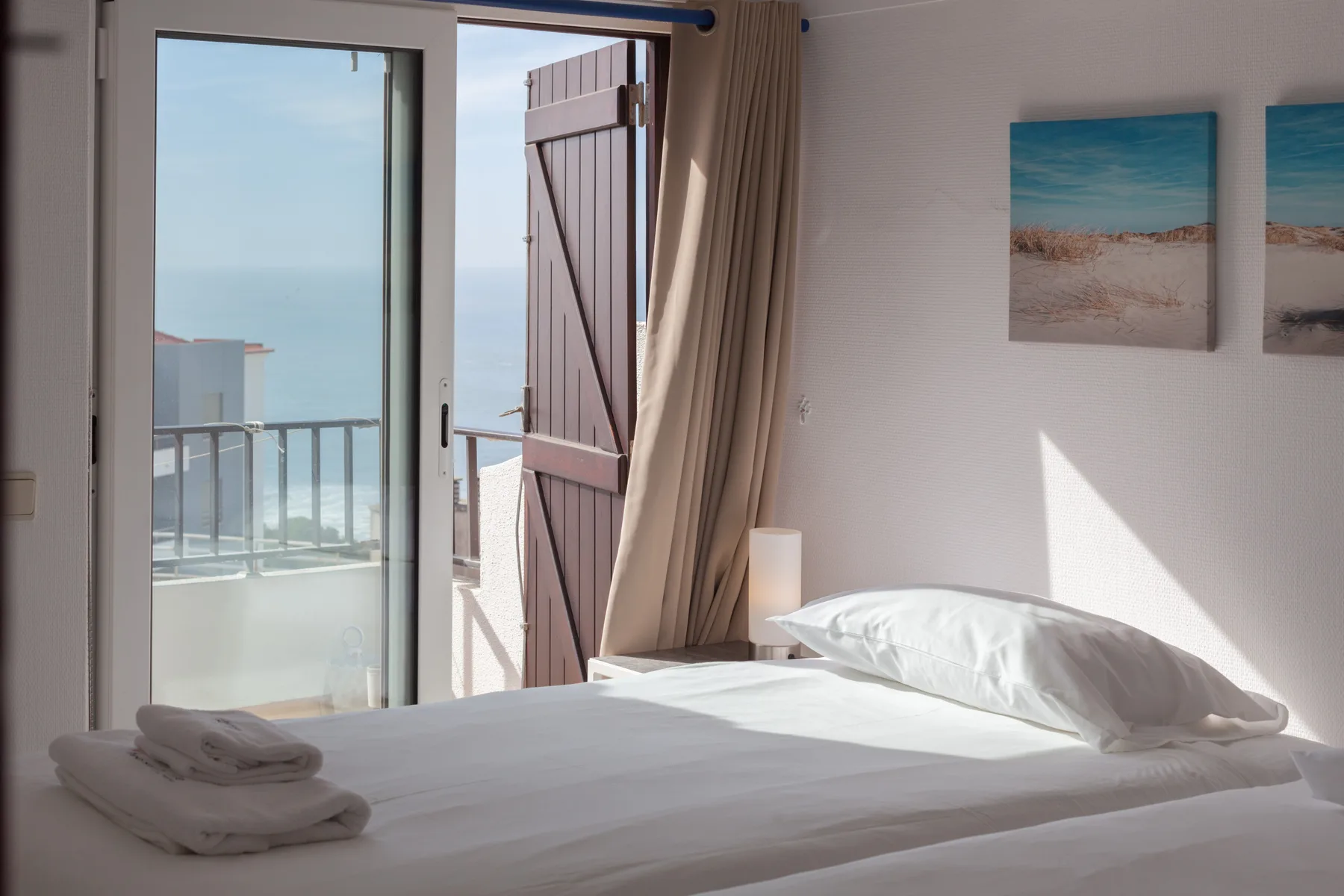 Un dormitorio con ropa de cama blanca da a un balcón con vistas al mar.
