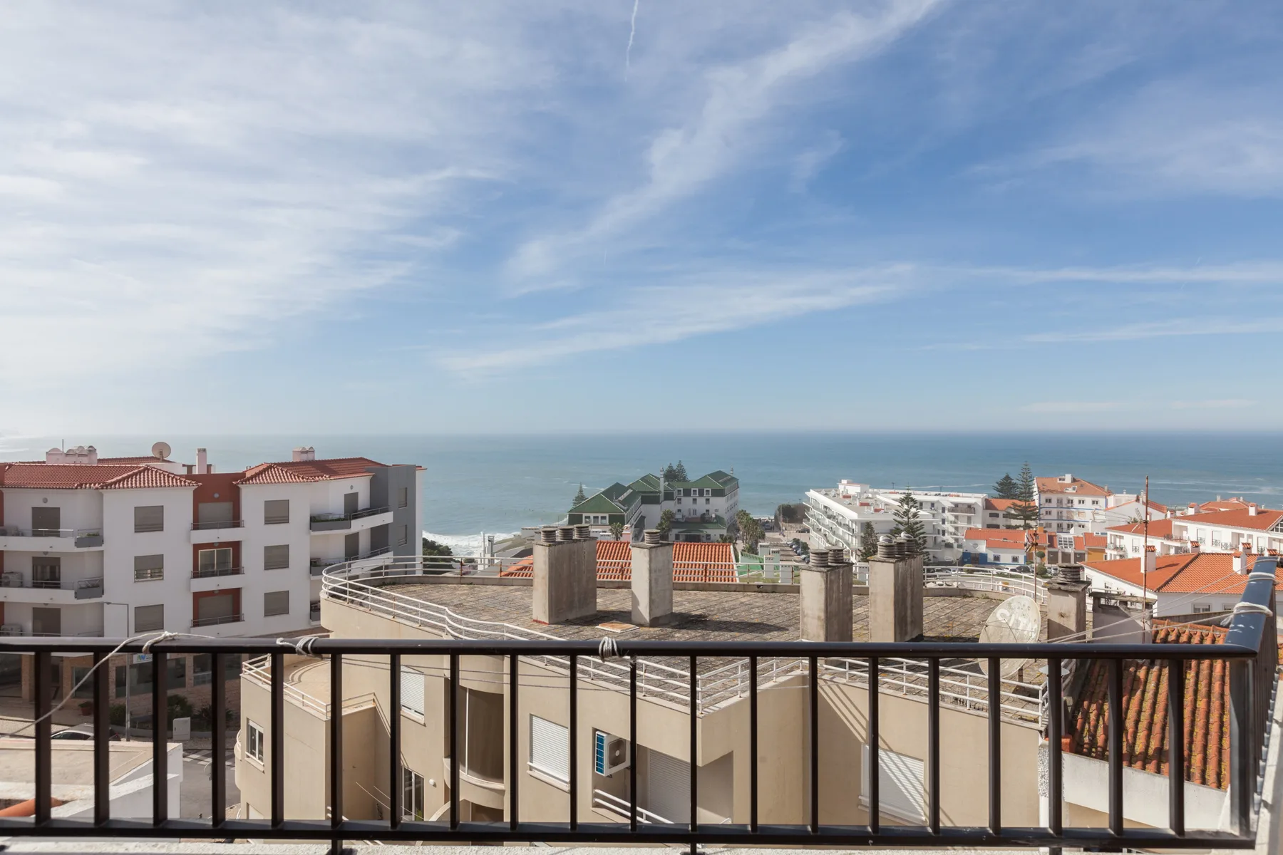 A balcony overlooks nearby buildings and the ocean beneath a cloudy sky.