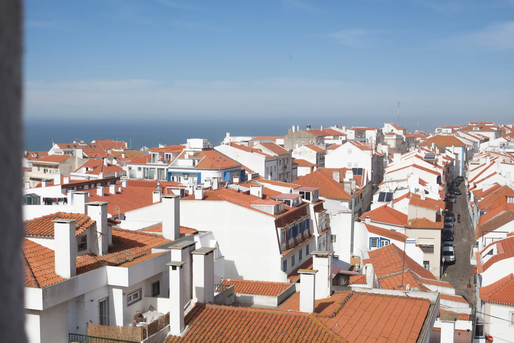 Edificios blancos con tejados de tejas rojas miran al mar bajo un cielo despejado.
