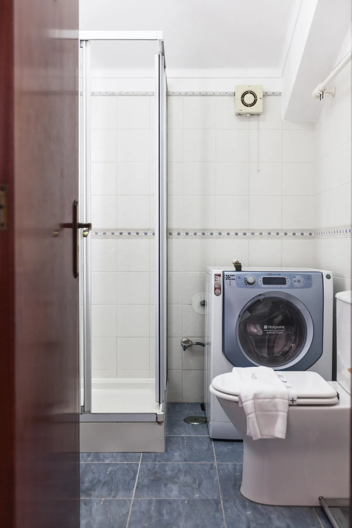 A tiled bathroom with a shower, washing machine, and toilet.