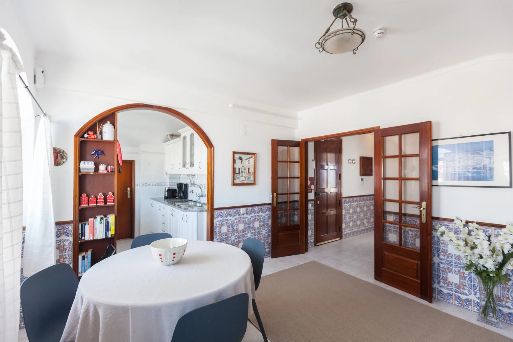 Dining area with a round table beside an arched opening and tiled walls.