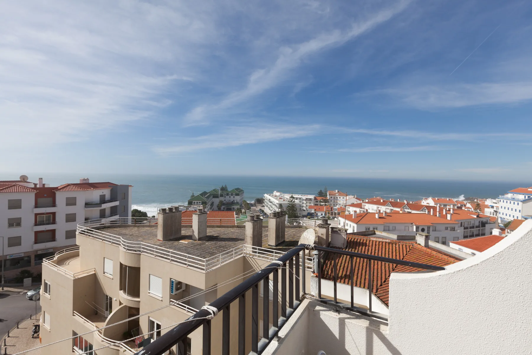 Una terraza en la azotea ofrece vistas de edificios cercanos y del océano bajo un cielo parcialmente nublado.