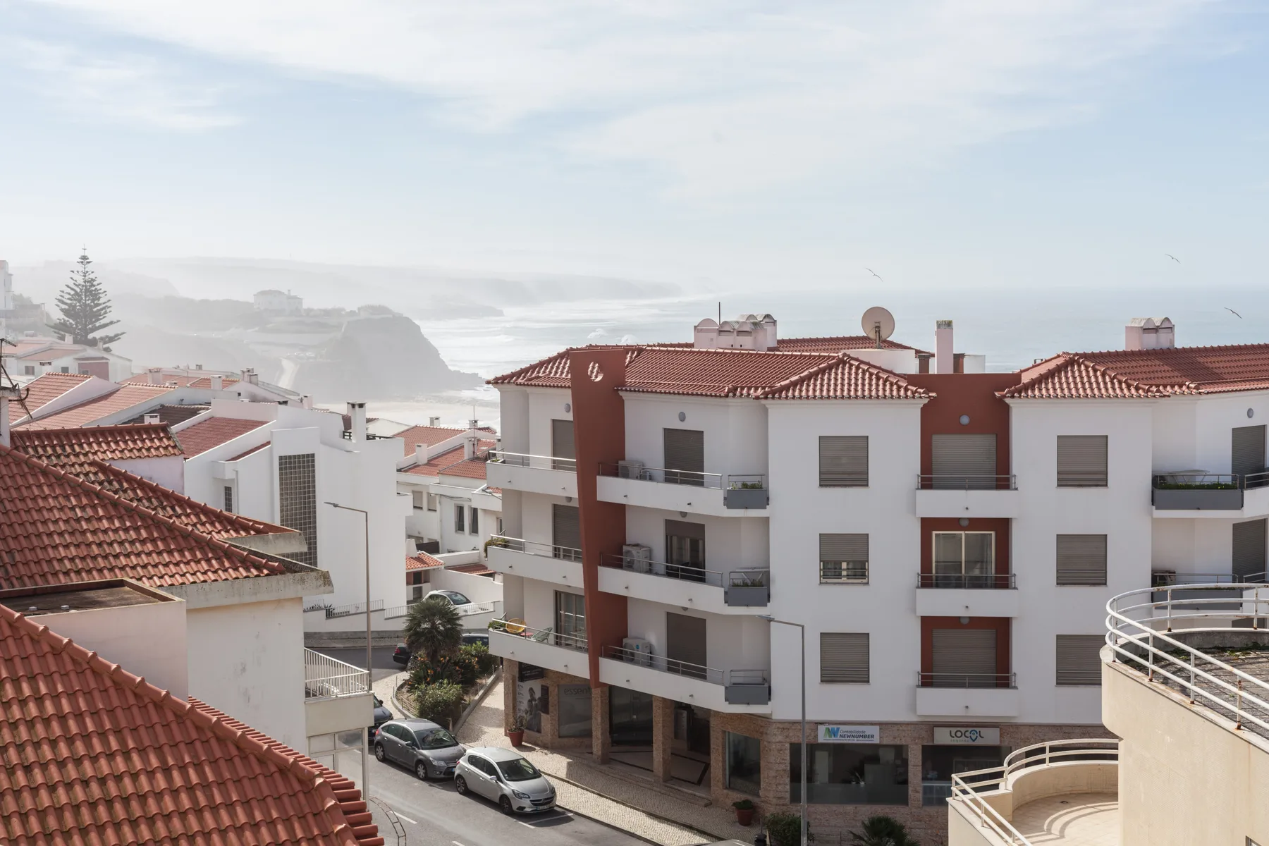 A coastal townscape with red-tiled rooftops and the sea in the distance.