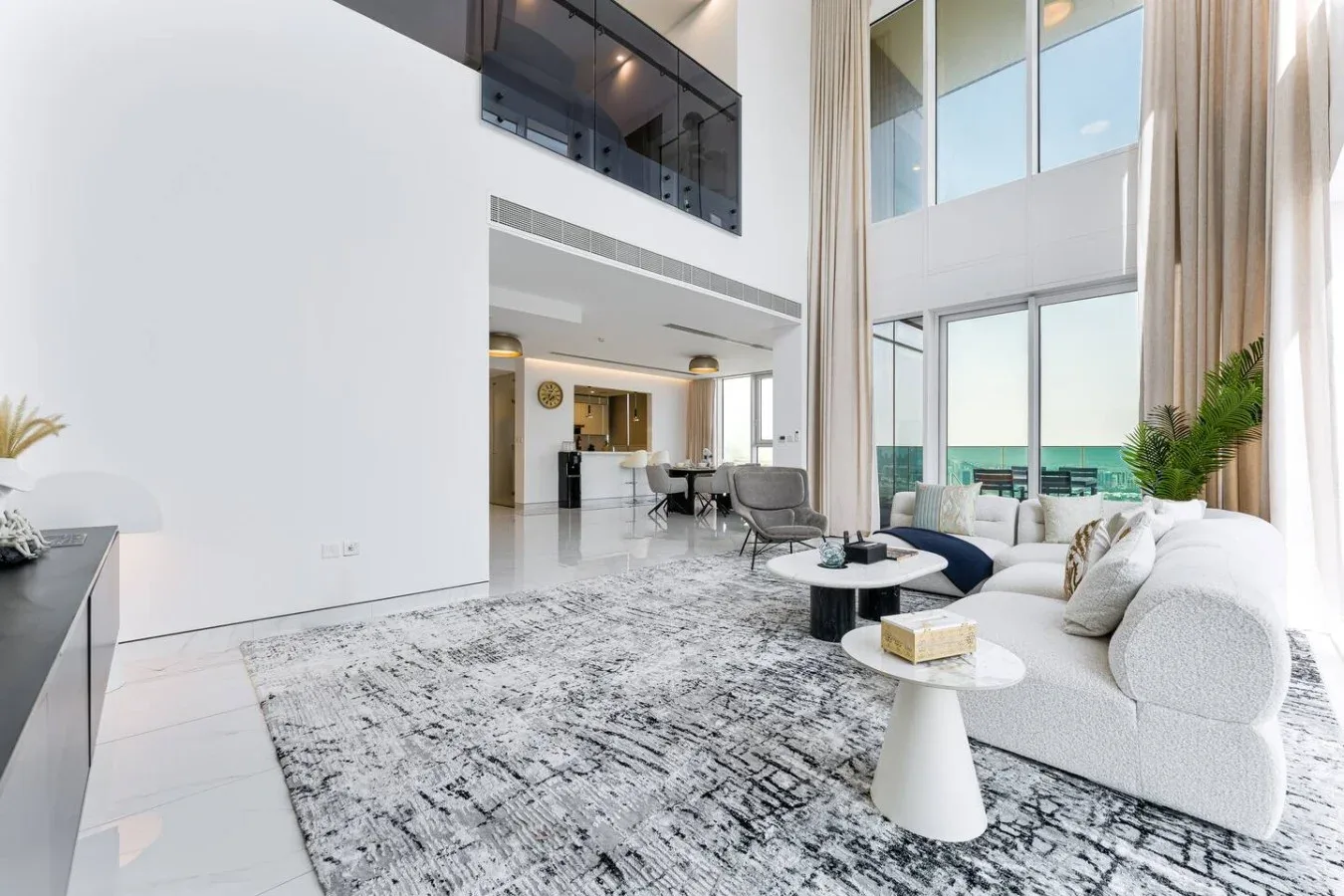 A bright double-height living room with large windows and a seating area.