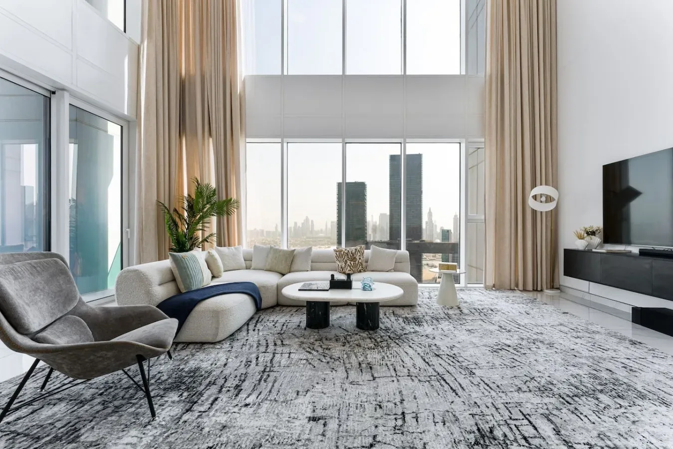 A bright living room with floor-to-ceiling windows, seating, and a low coffee table.