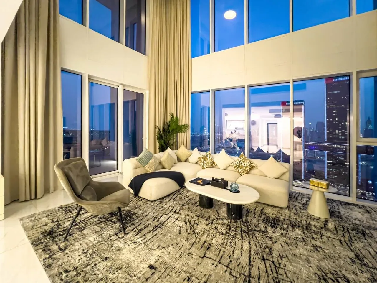 A bright living room with seating beside tall windows overlooking the city.