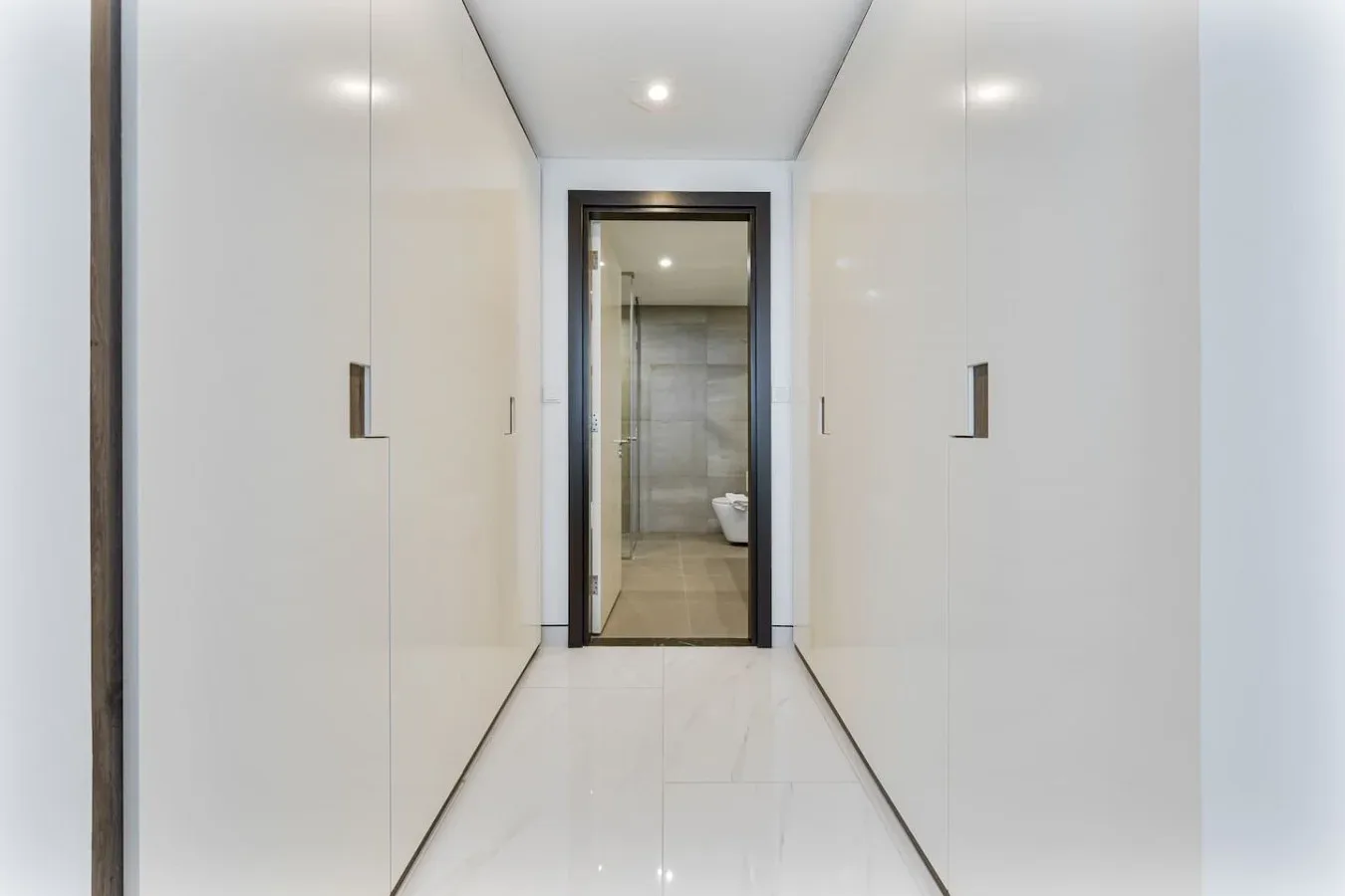 A bright hallway lined with white built-in cabinets leads to a bathroom.