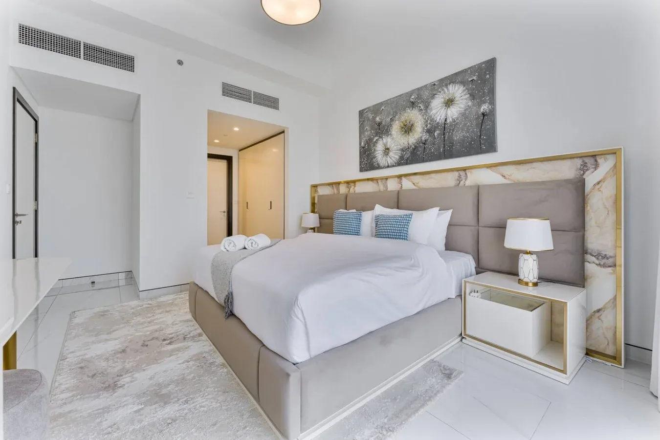 A bright bedroom with a large bed, bedside tables, and floral wall art.