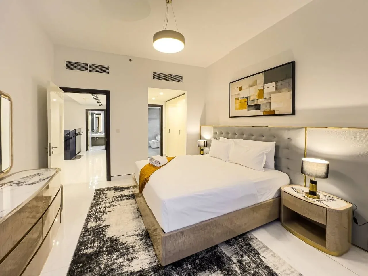 A bedroom with a made bed, bedside tables, and abstract wall art.