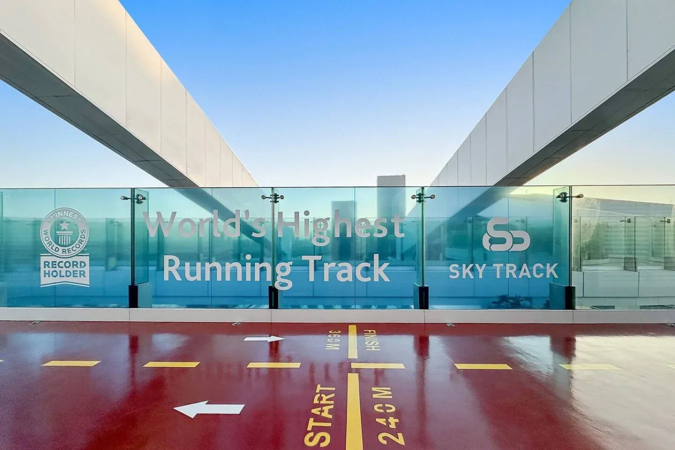 A running track with painted start markings and a glass barrier beneath a clear sky.