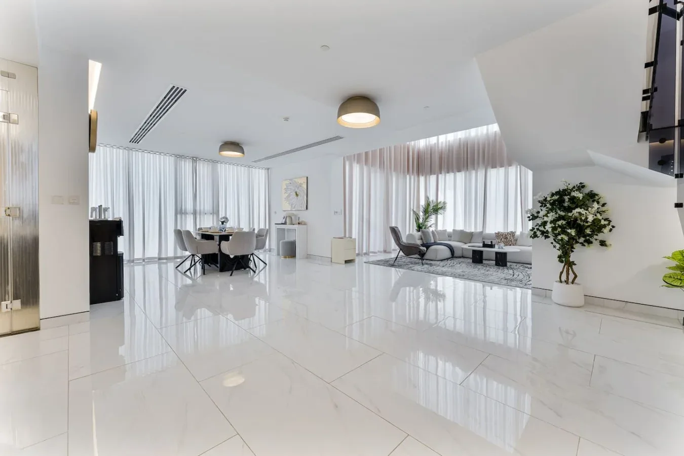 A bright living and dining area with seating, a table, and large windows.