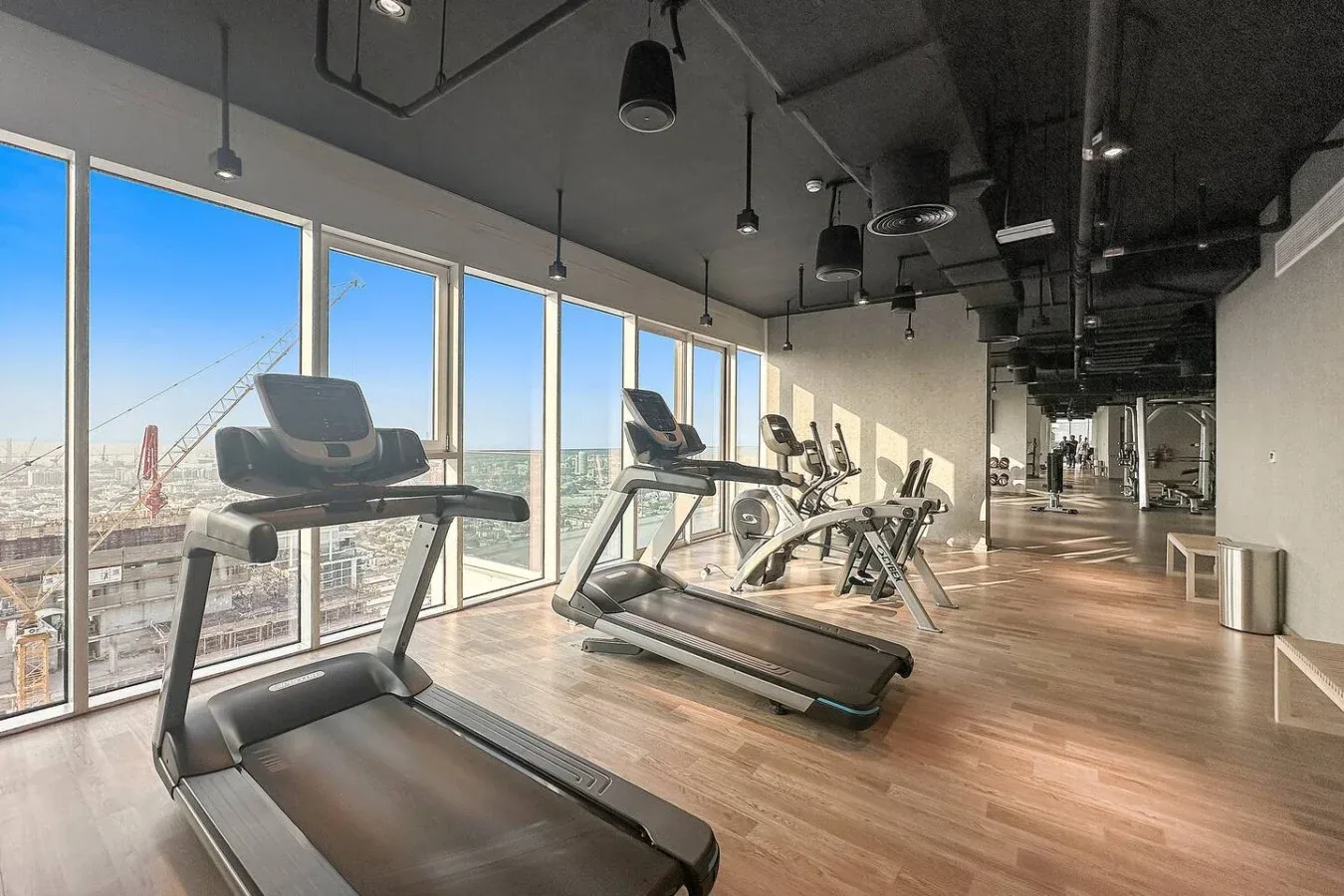 A gym with treadmills and exercise equipment beside large windows.