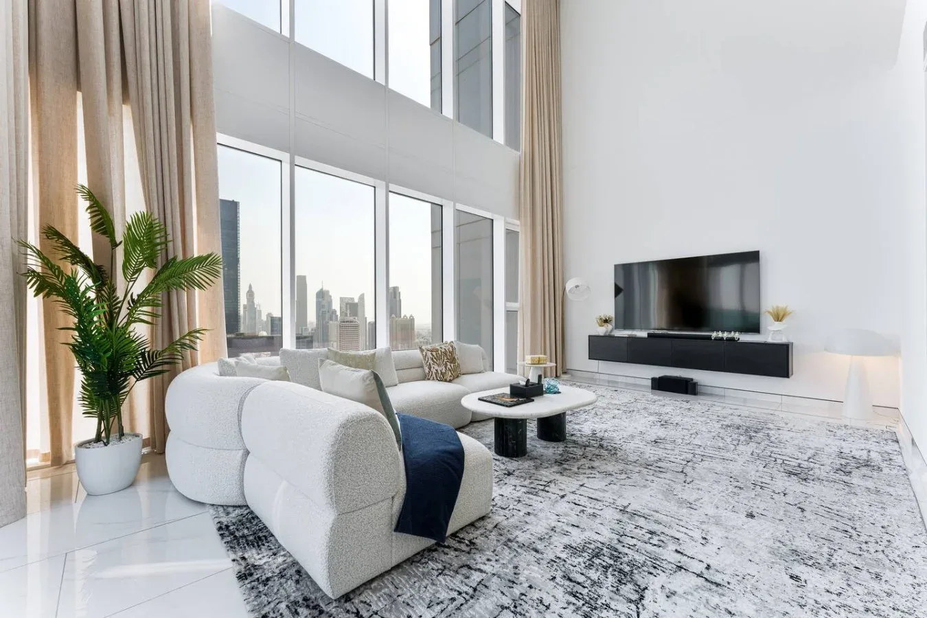 A bright living room with large windows, seating, and a television.