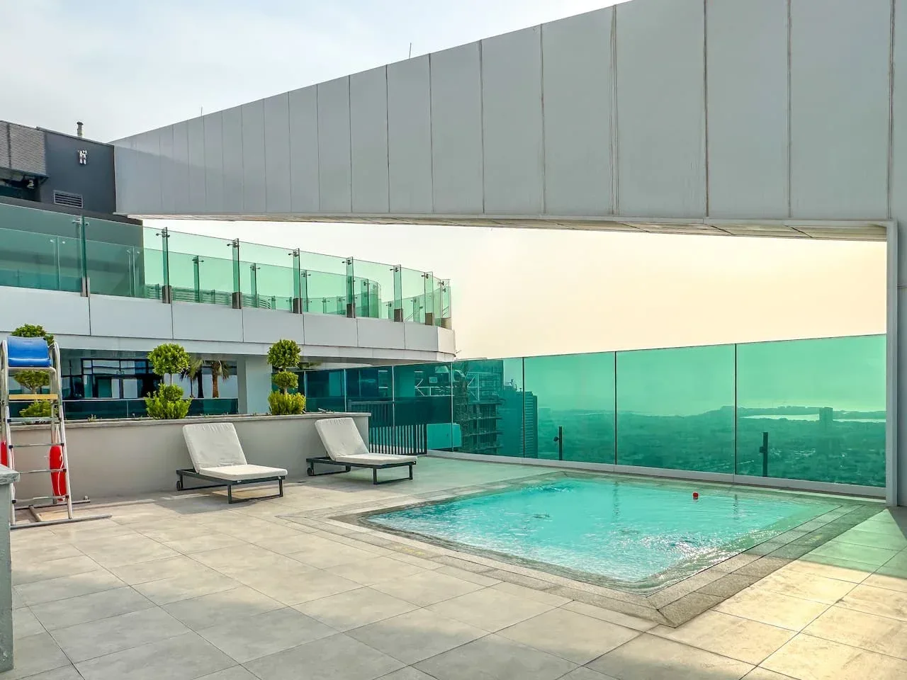 A rooftop swimming pool sits beside a glass railing overlooking the surrounding city.