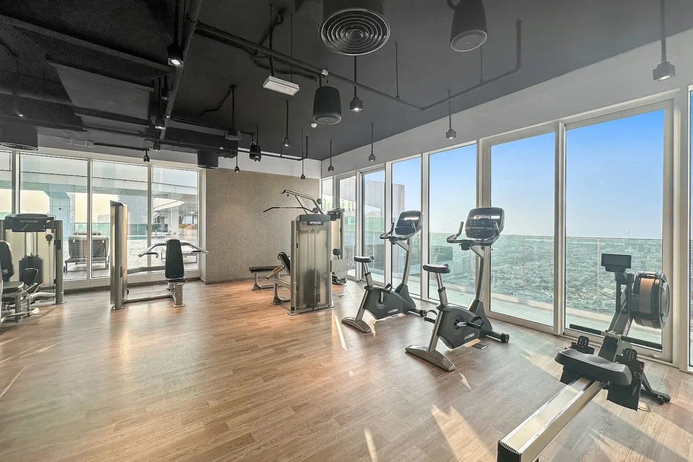 A gym with exercise bikes and strength-training equipment beside large windows.