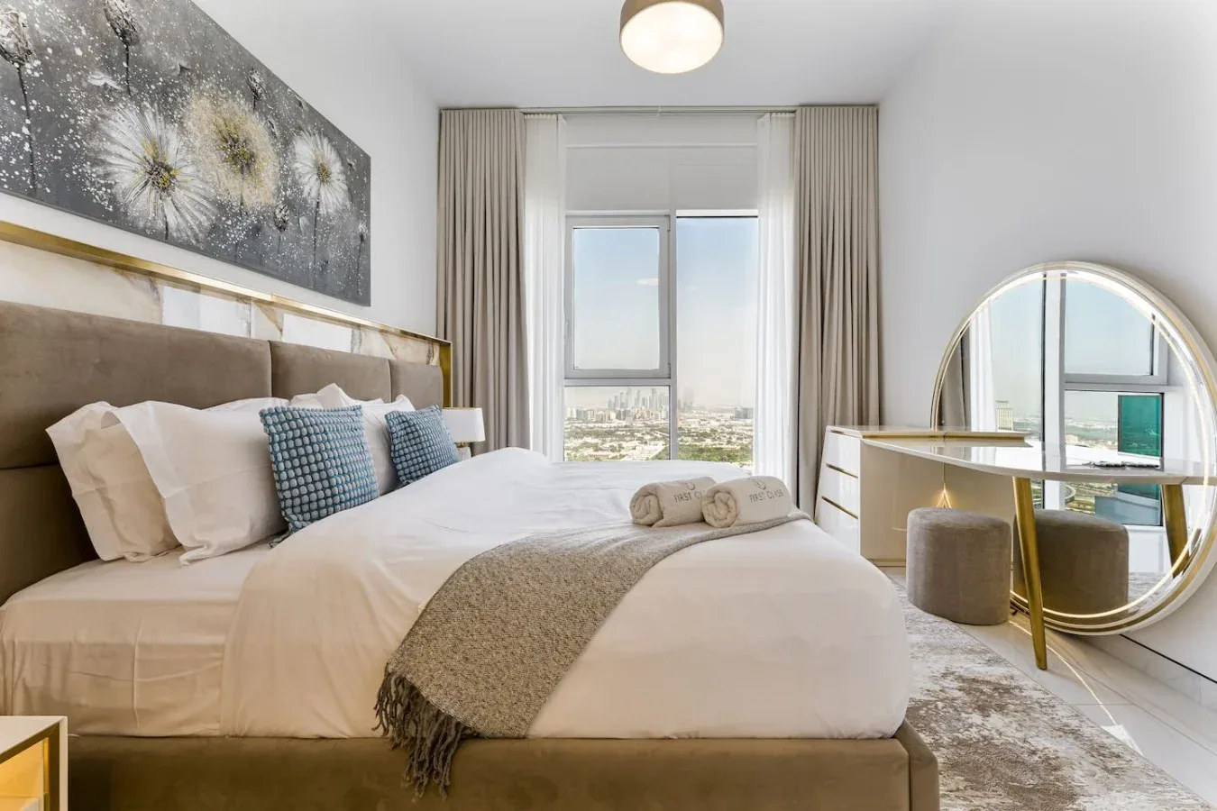 A bedroom with a neatly made bed, framed artwork, and a large window.