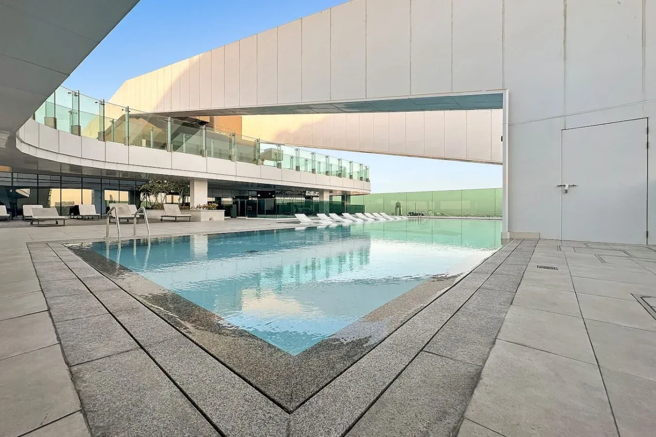 An outdoor swimming pool beside a modern building and paved deck.