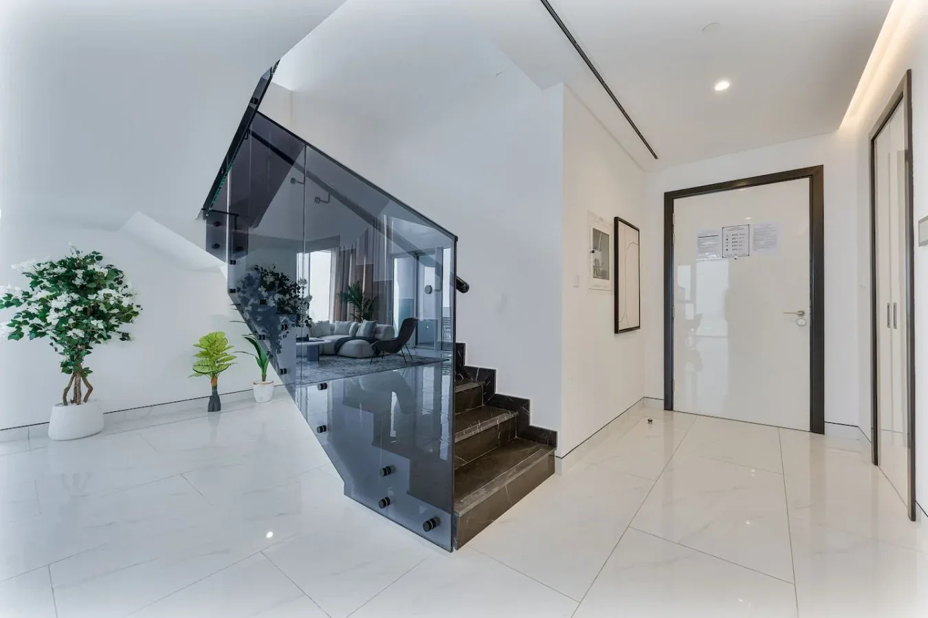 A bright modern entry hall with a staircase enclosed by glass panels.