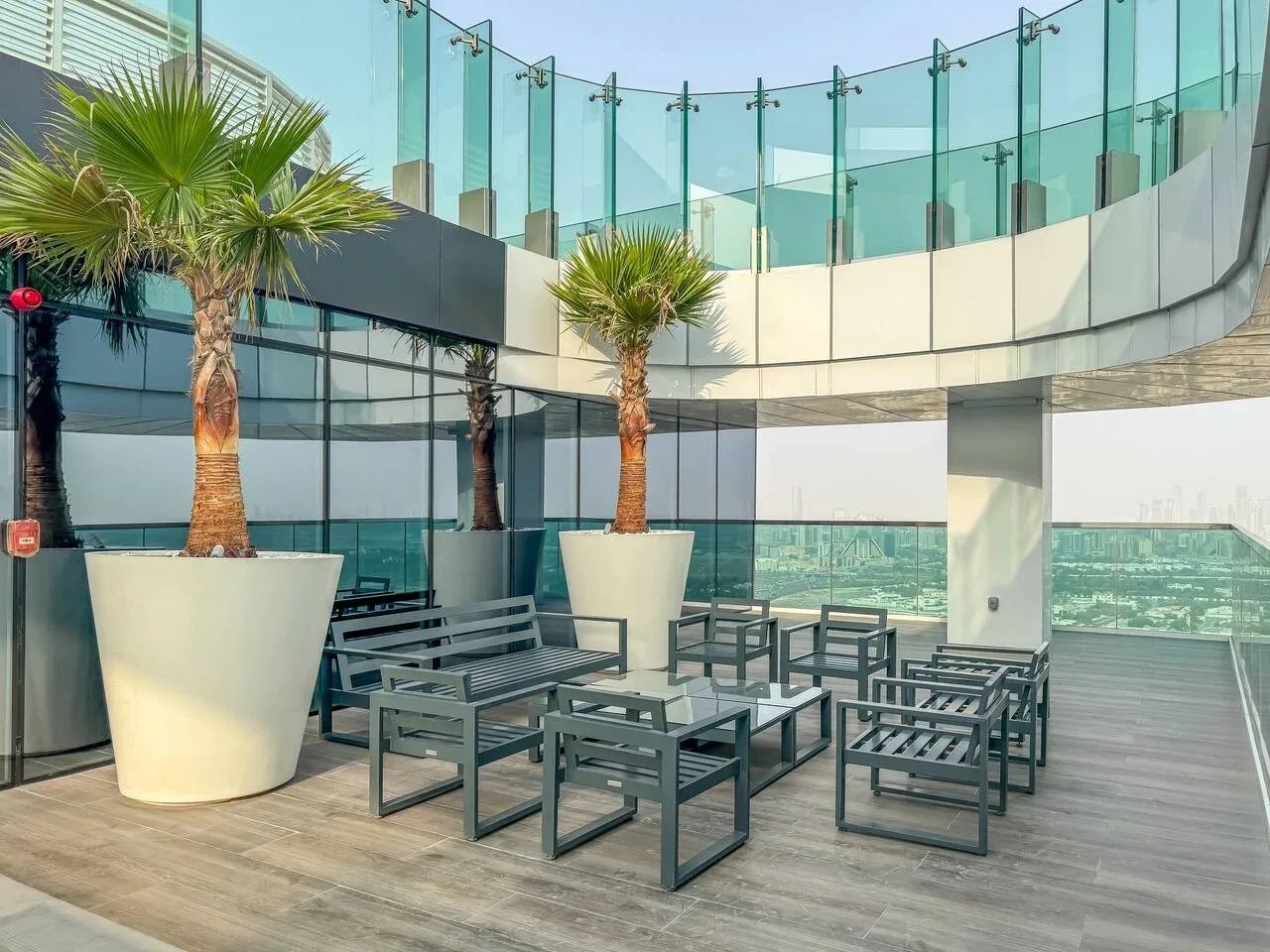 An outdoor terrace with seating, potted palms, and glass railings.