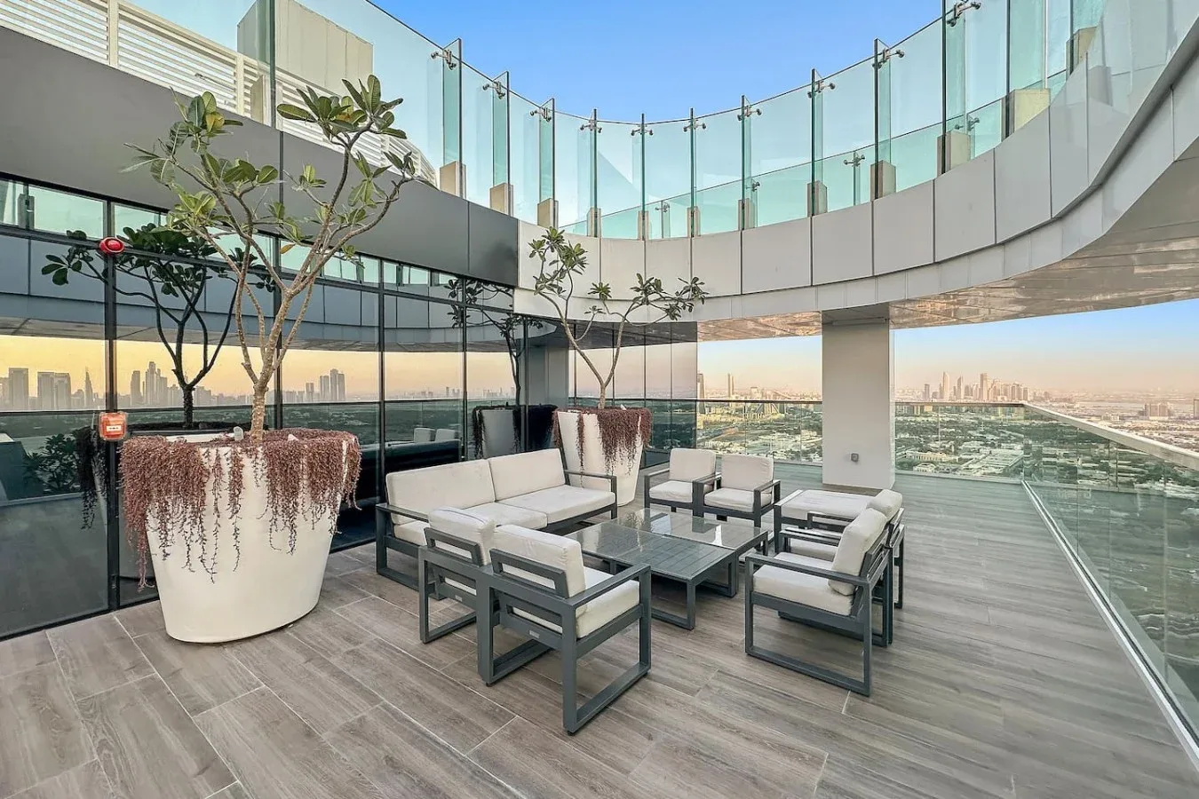 Outdoor seating area on a terrace with glass railings and a city view.
