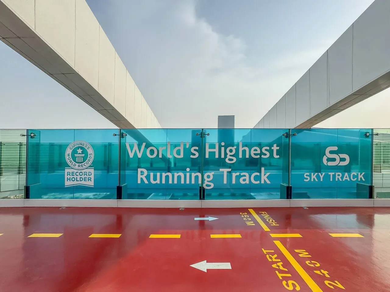 A rooftop running track with a red surface and turquoise glass panels.