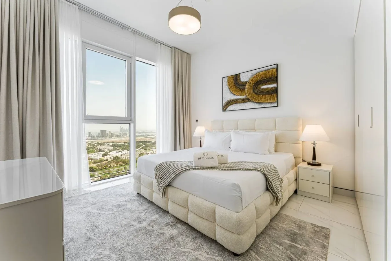 A bright bedroom with a large bed beside tall windows.