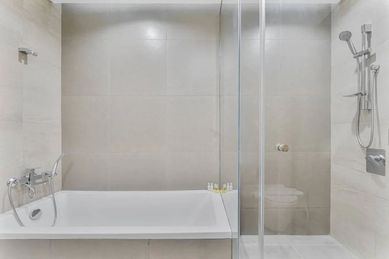 A tiled bathroom with a bathtub, glass shower, and wall-mounted shower fixtures.