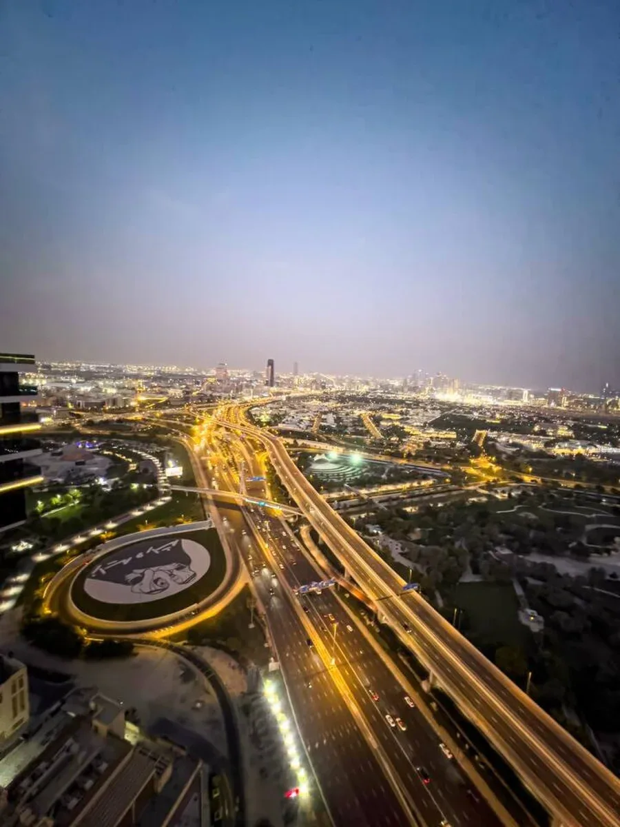 A nighttime cityscape overlooks illuminated highways and a distant skyline.