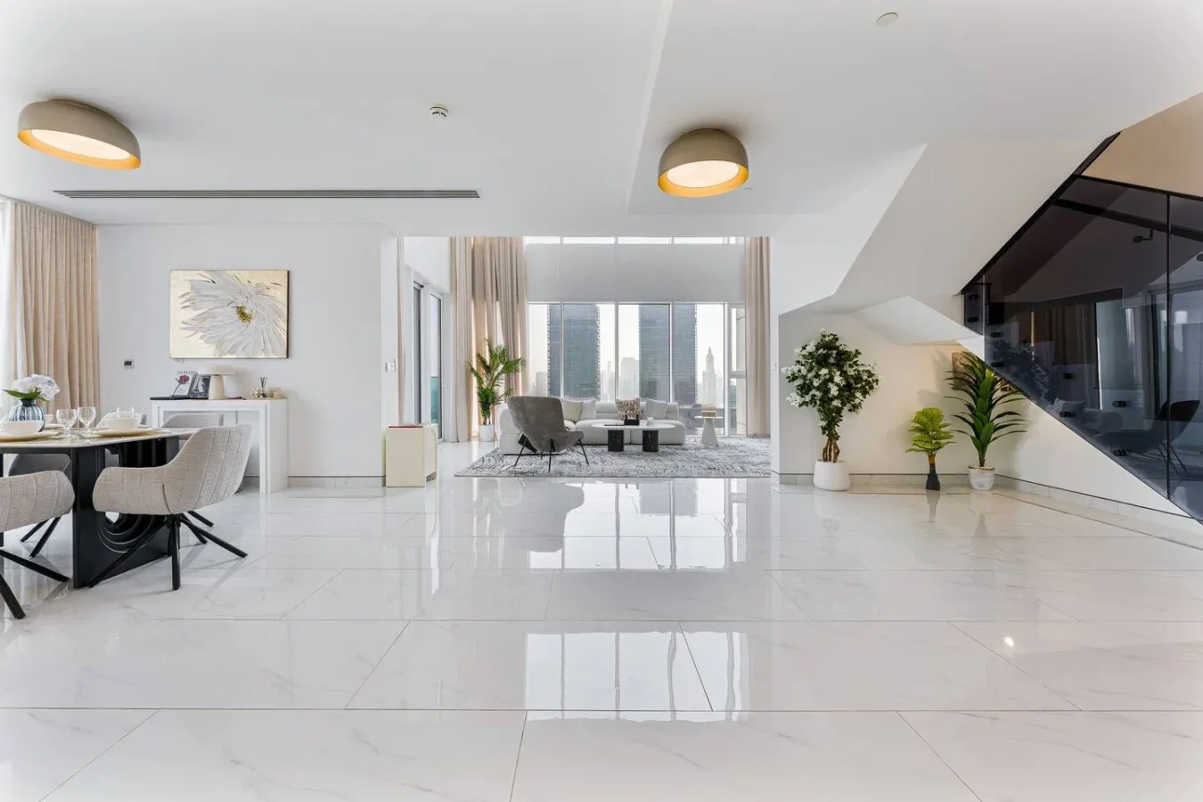 A bright open-plan living and dining area with large windows and indoor plants.