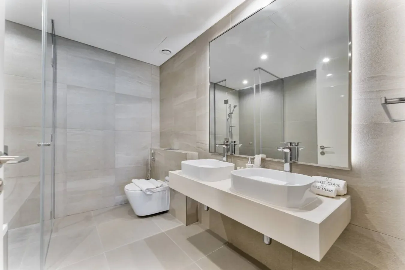 A bright tiled bathroom with a double sink vanity and a shower.