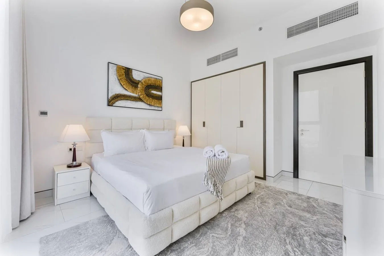A bright bedroom with a neatly made bed and framed artwork above it.