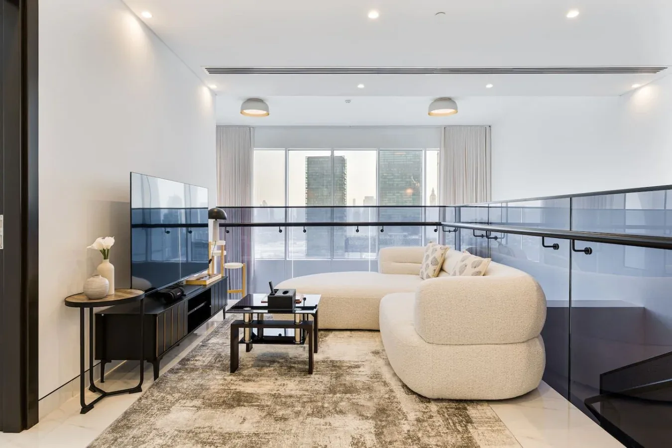 A bright living room with curved seating, a television, and large windows.