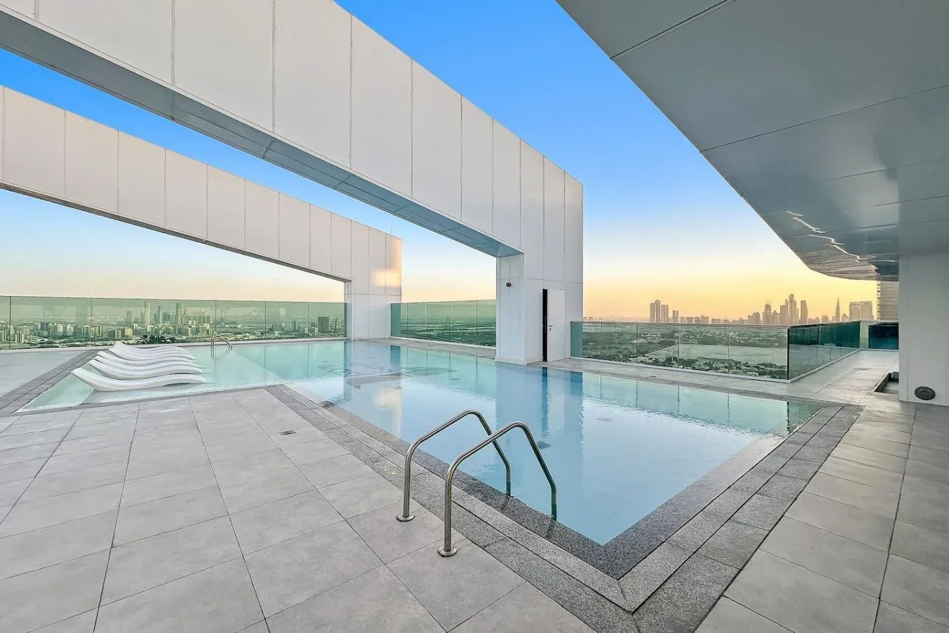 A rooftop swimming pool overlooks the city skyline at sunset.