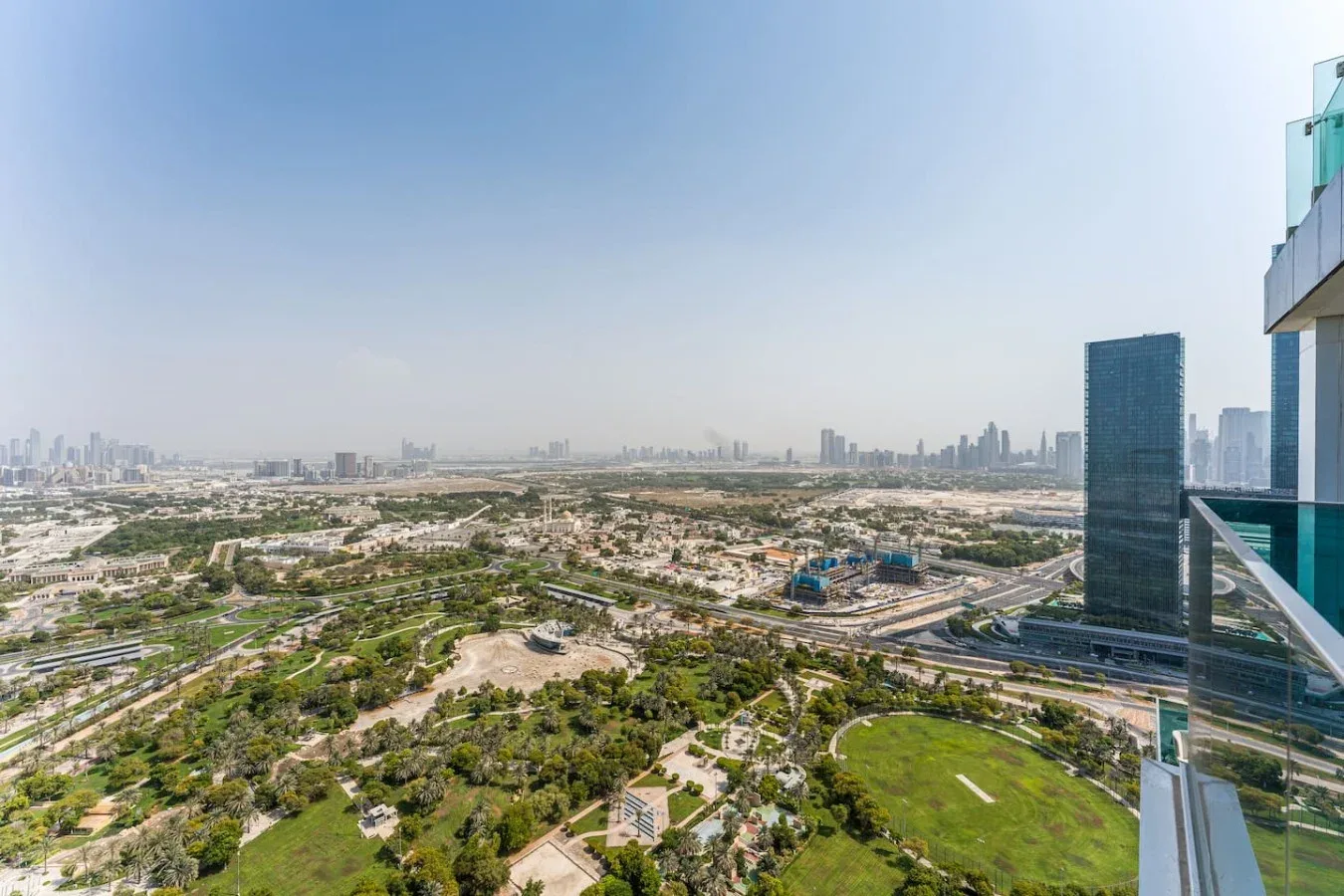 An expansive city skyline rises beyond green parkland and winding roads.