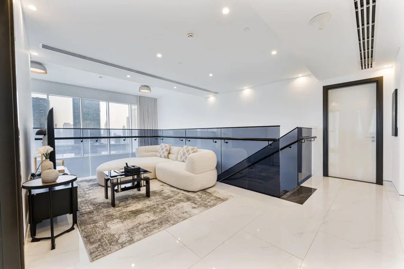 A bright living area with seating, a rug, and a glass railing beside the stairs.